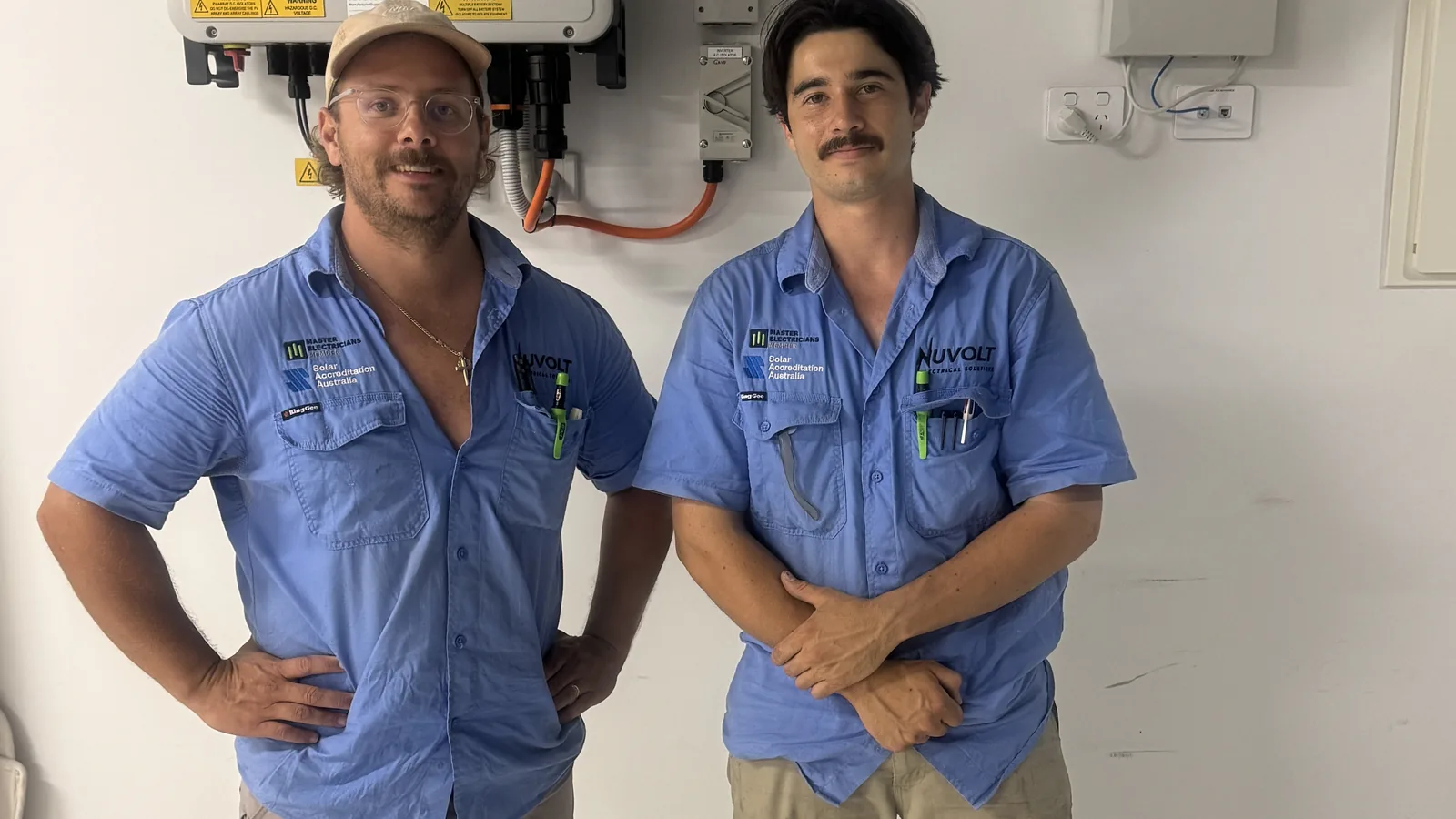 Two licensed Nuvolt electricians on site in front of an installed inverter and switchboard