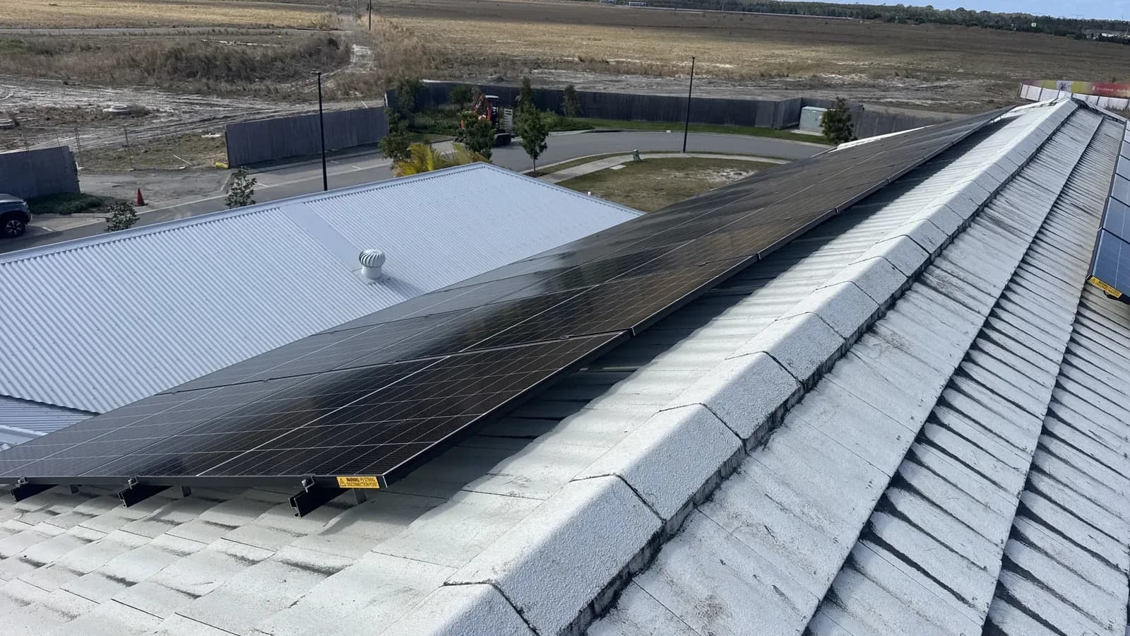 A rooftop solar array on a tiled roof on the Sunshine Coast, installed by Nuvolt, with the DC isolator warning label visible on the rail