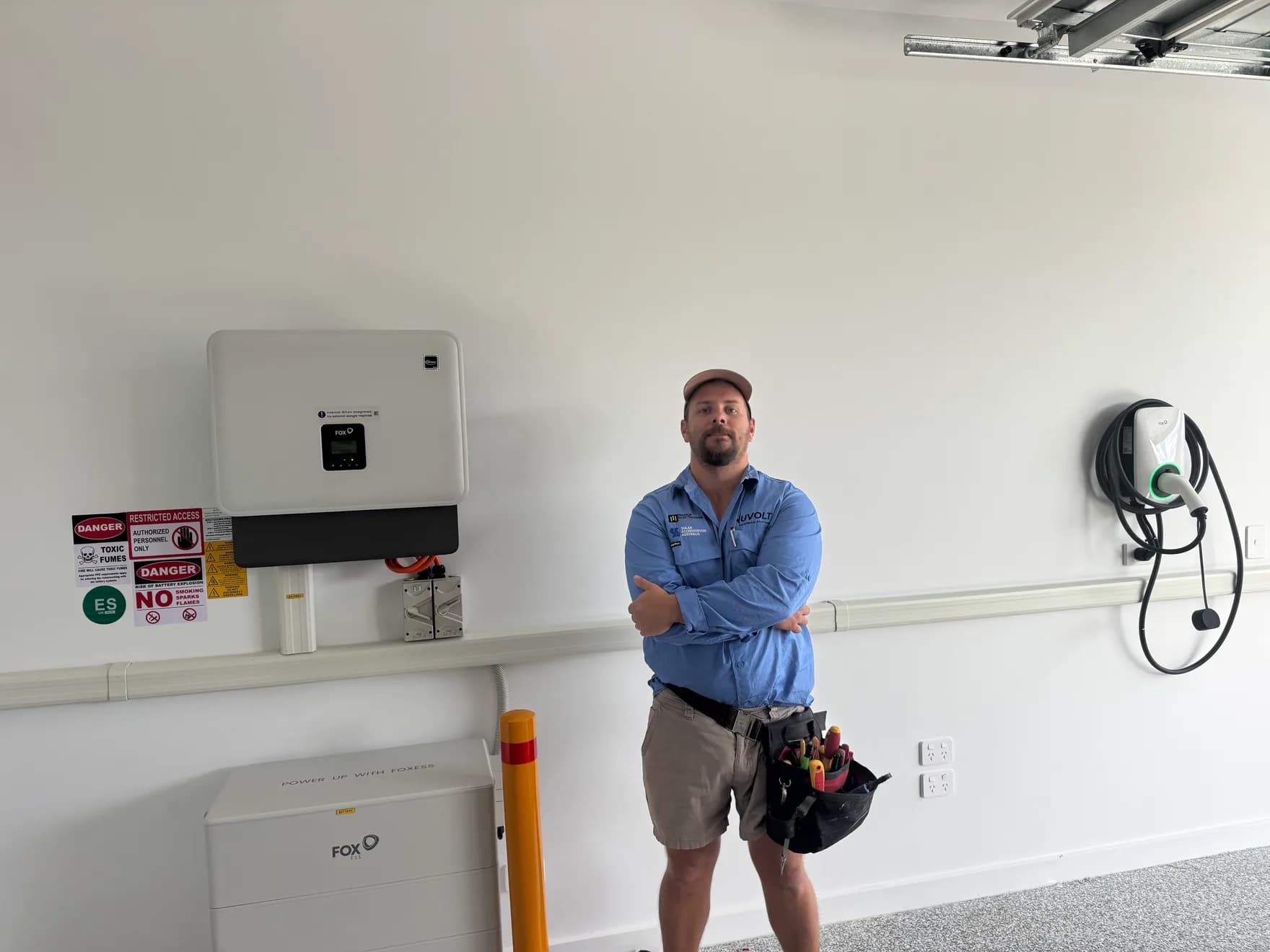 Nuvolt electrician beside a completed Fox ESS hybrid inverter, home battery and EV charger installed together in one Sunshine Coast garage