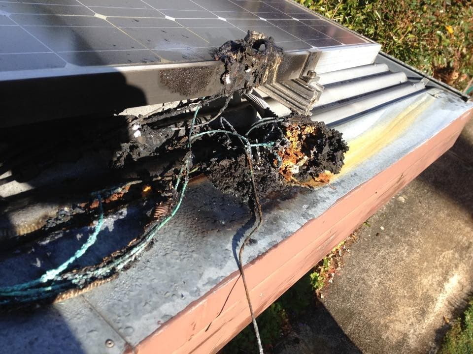 A rooftop solar DC isolator that has burnt out at the edge of a solar panel, with charred conductors visible
