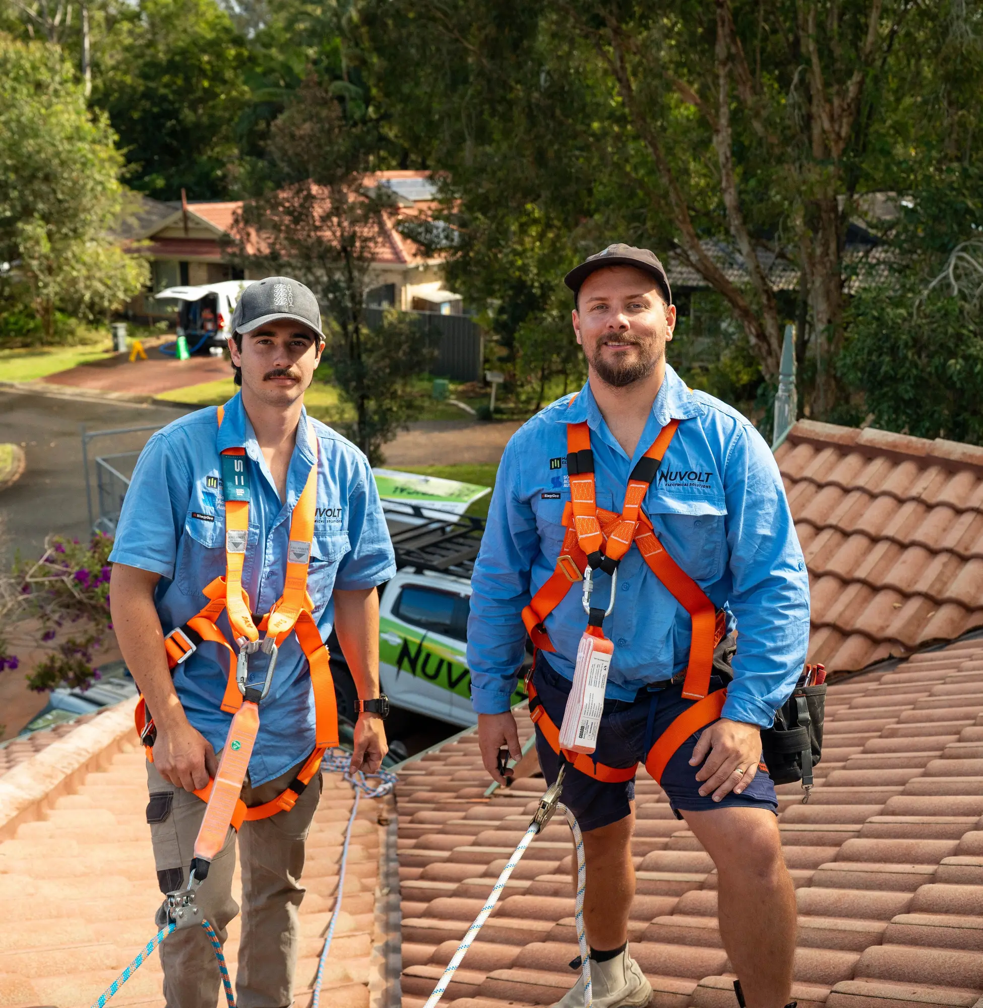 Dan and a Nuvolt team member in safety harnesses on a tiled roof, with the Nuvolt ute parked below