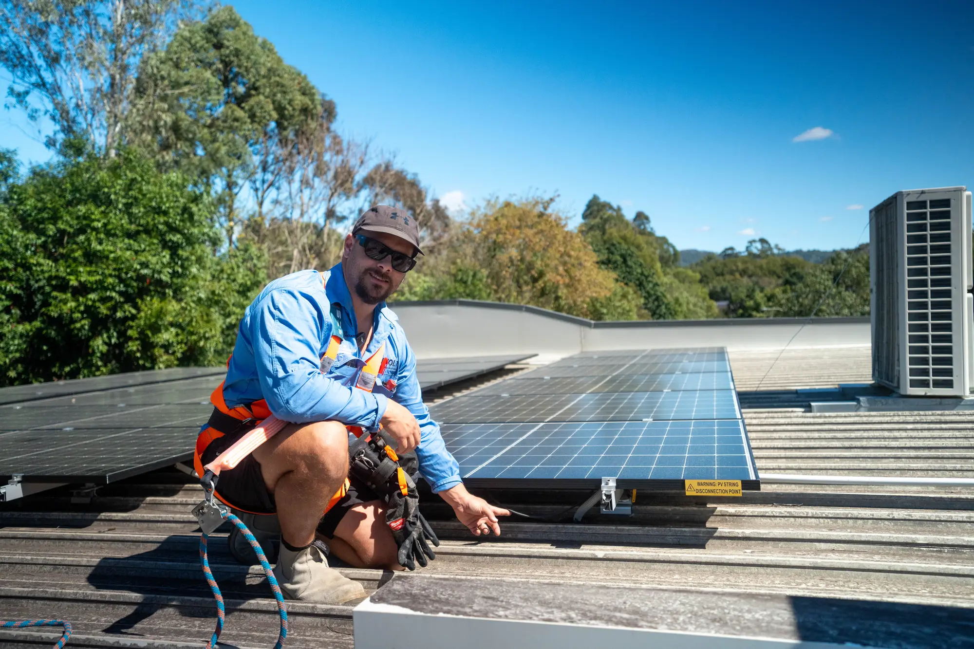 Dan from Nuvolt in a safety harness, crouched beside a row of rooftop solar panels