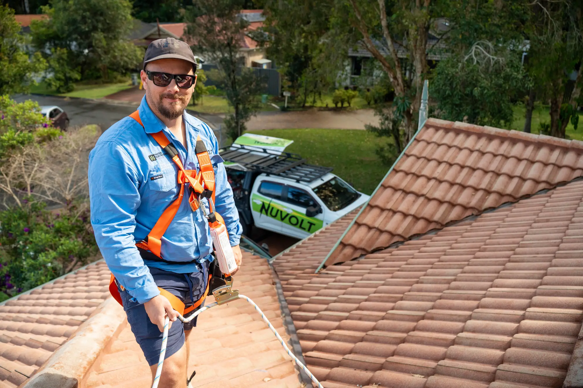 Dan from Nuvolt on a tiled roof in a safety harness, clipped to a rope line